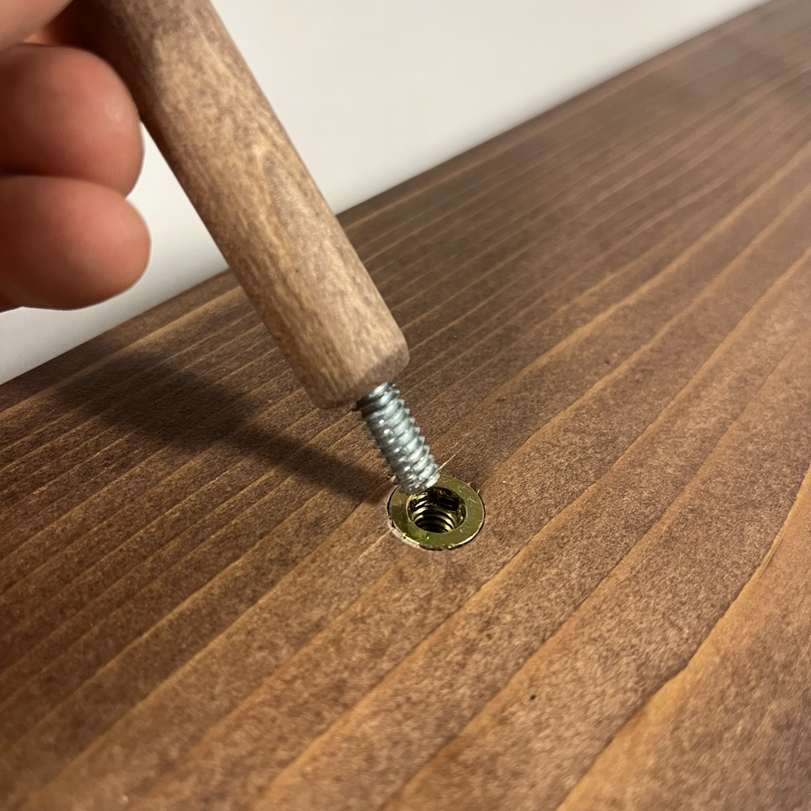 Close-up of a hand guiding a threaded rod to be screwed into a bagel stand base.