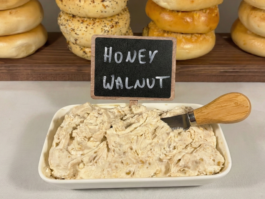 A close-up of a schmear tray with spreading knife in cream cheese in front of bagel stand.