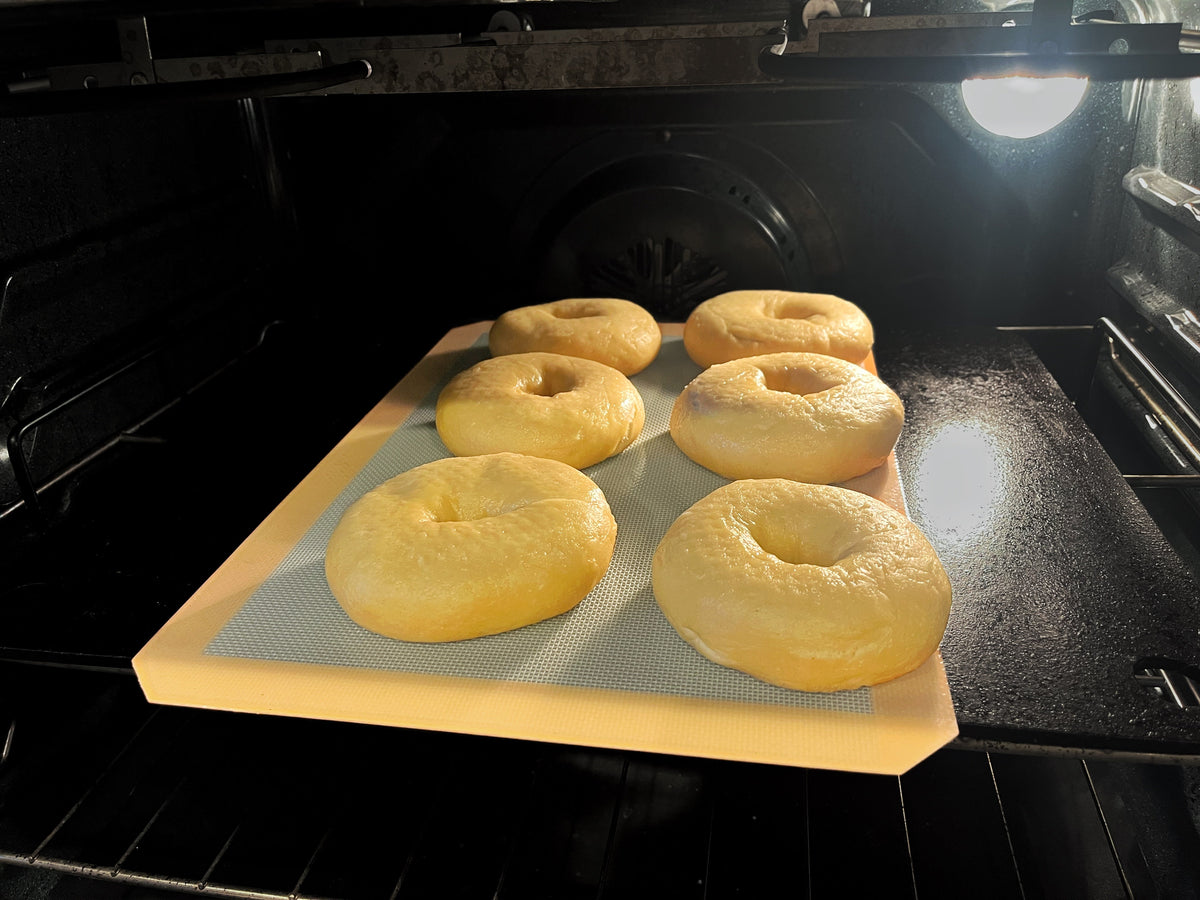 Raw bagels in the oven on baking steel with a baking mat.
