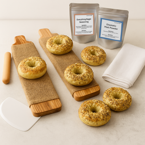 Cedar bagel boards arranged with everything bagel seasoning, bagel mix, malt powder, and tools on a white countertop.