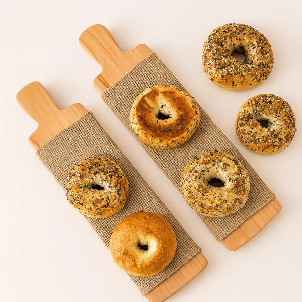 Two cedar bagel boards with snap-on burlap covers, raw bagels arranged on top.