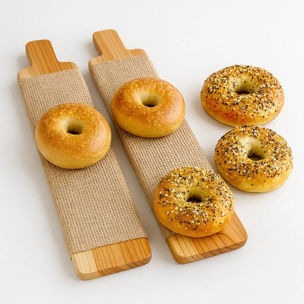 A pair of cedar bagel boards on a white countertop with raw bagels resting on top.