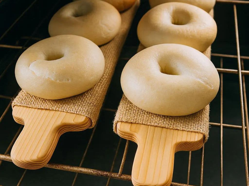 Two cedar bagel boards loaded with raw bagels in a hot oven, showing the bagel boards in use.
