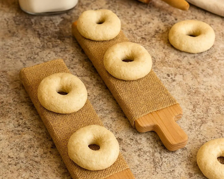 Raw bagels loaded on bagel boards on countertop with ingredients and tools.